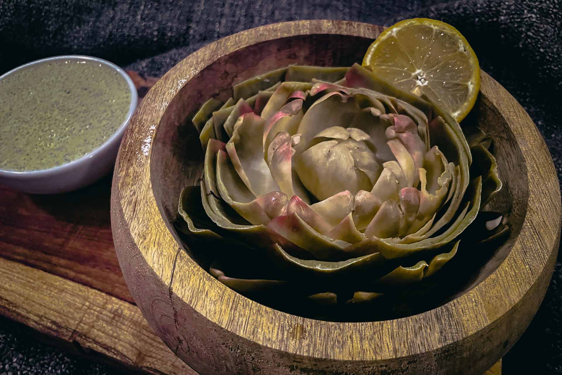 Artischocke in einer Holzschüssel serviert mit Zitrone und Vinaigrette