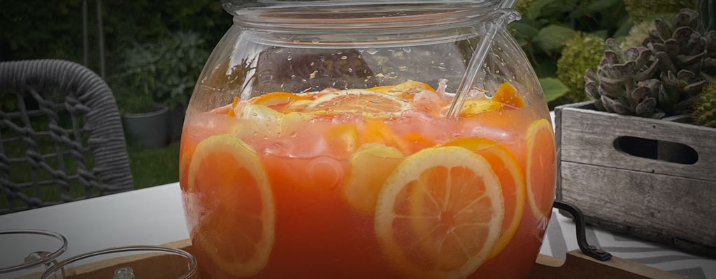 Campari Milano Punch in einer Glasbowle im Freien auf einer Gartenparty, leuchtend orange Orangenscheiben und Eiswürfel