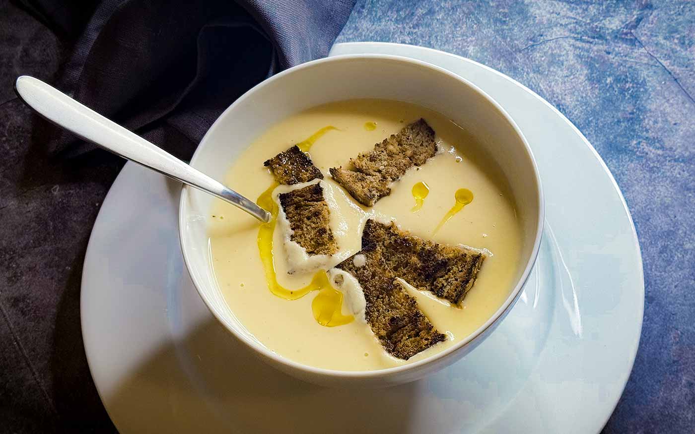 Erdäpfel-Sellerie-Suppe mit Trüffelöl und geröstetem Schwarzbrot in einer weißen Suppenschale