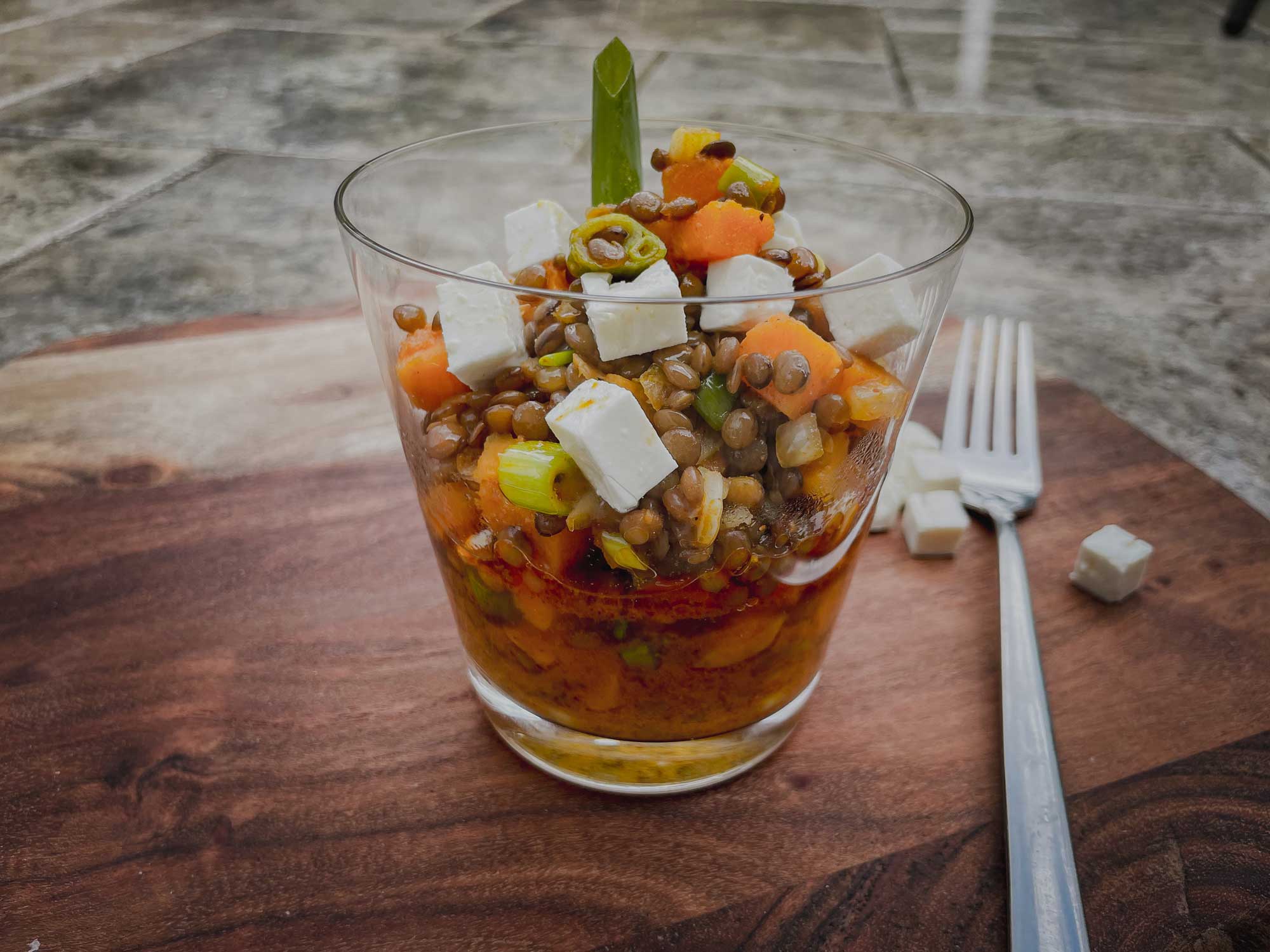 Salat aus grünen Linsen, Süßkartoffel, Jungzwiebel und Feta im Glas serviert auf einem Holzbrett