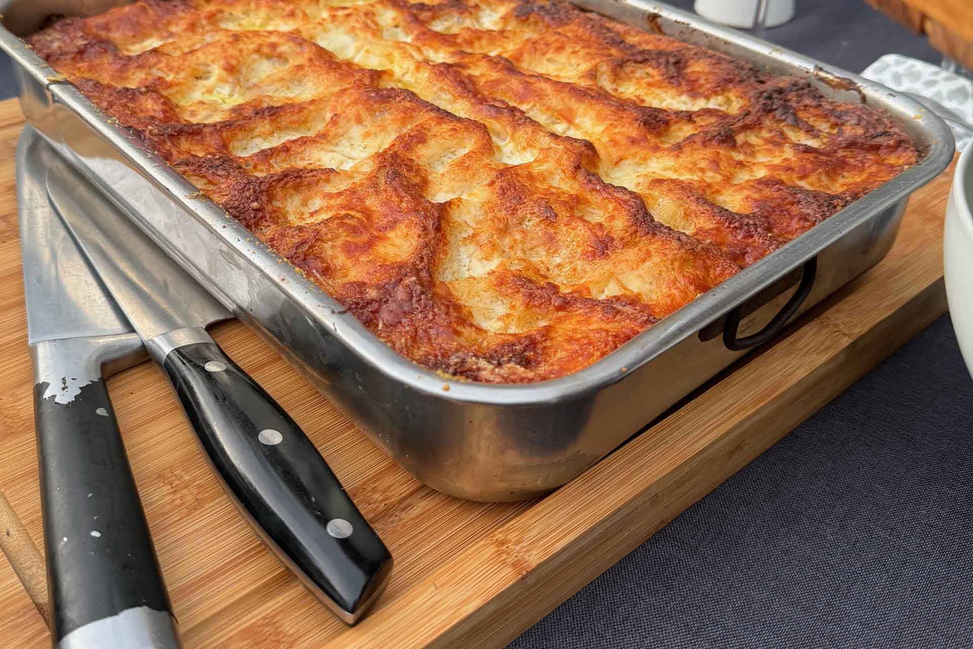 Vegetarische Lasange mit roten Linsen in einer Auflaufform auf einem Holzbrett