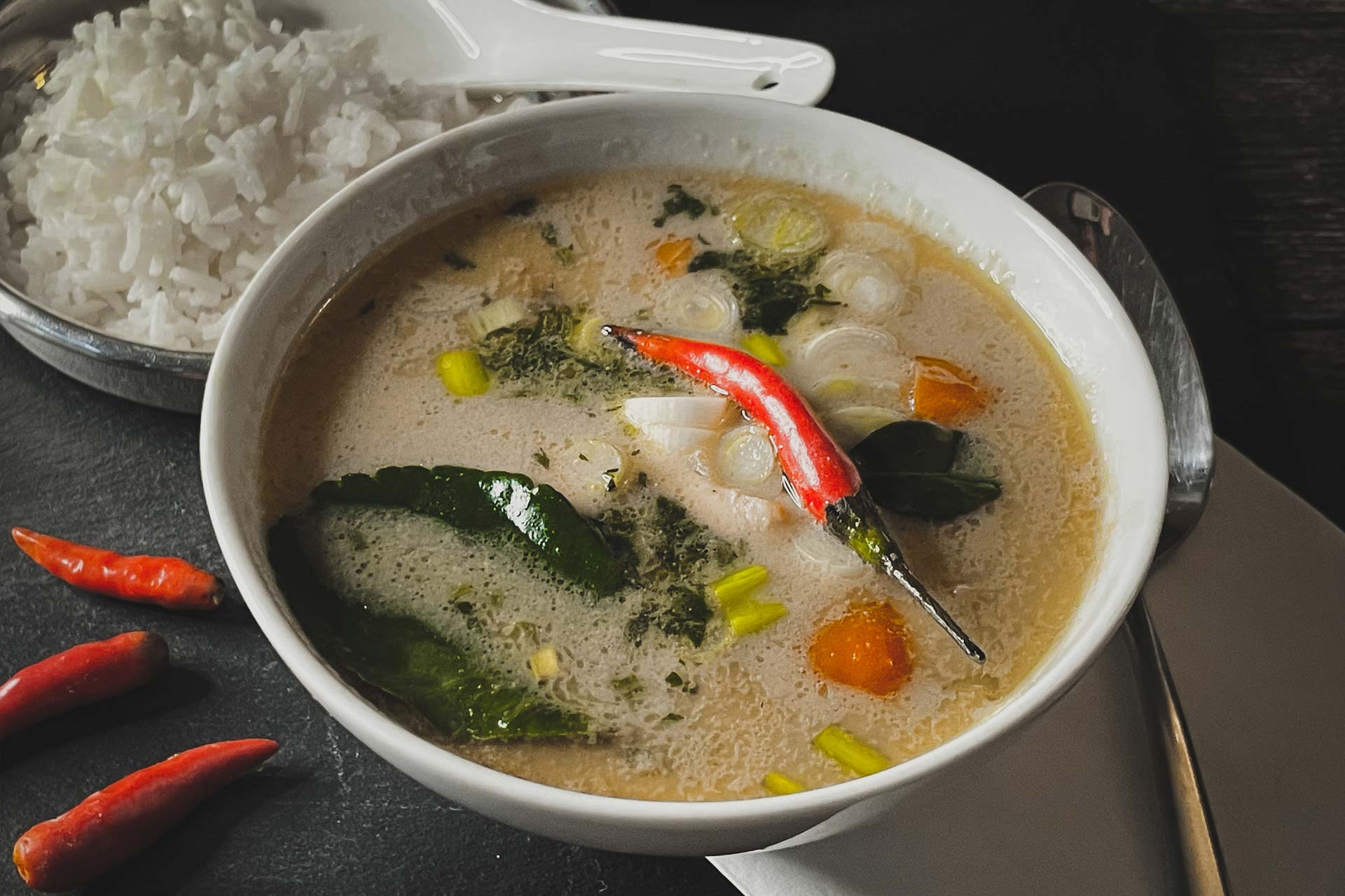 Tom Kha Gai, thailändische Kokossuppe mit roten Chilis, Kaffirlimettenblätter, Jungzwiebel, Koriander und Fischsauce